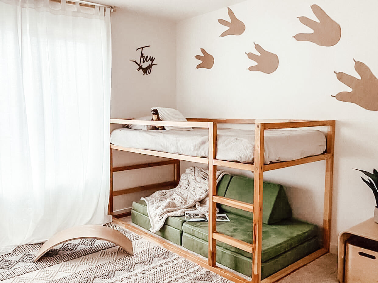 Dinosaur personalized wooden name sign next to wooden bunkbed and dinosaur feet covering the wall.
