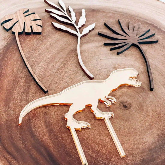 Dinosaur party pack, gold T-REX cake topper displayed on a piece of wood.