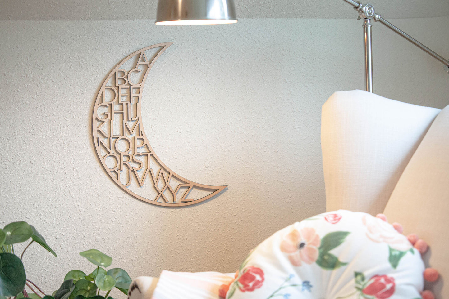 wooden alphabet moon nursery decor next to white chair, a lamp that's on, and a green plant