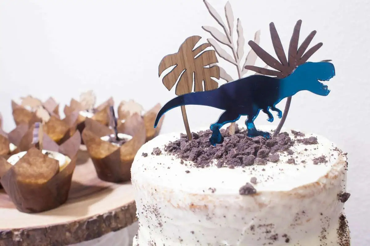 Dinosaur party pack, teal T-REX cake topper displayed on cupcakes and a cake.