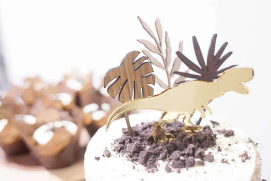 Dinosaur party pack, gold T-REX cake topper displayed on cupcakes and a cake.
