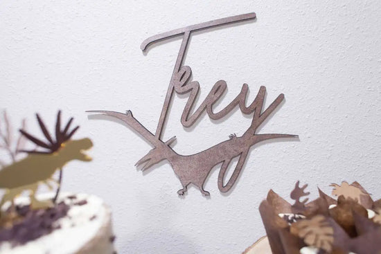 Load image into Gallery viewer, Dinosaur party pack, gold T-REX cake topper displayed on cupcakes and a cake, with custom name sign with dinosaur hanging on the wall.
