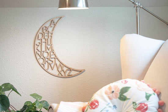 wooden alphabet moon nursery outlet decor next to white chair, a lamp that's on, and a green plant