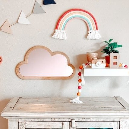 Pink cloud mirror, nursery wall decor next to shelf with boho decor.