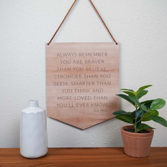 wooden nursery quote hanging on a white wall with green plants