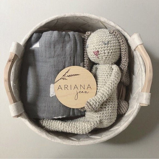 Botanical engraved wooden baby sign inside a nursery basket filled with a stuffed bunny and blanket.