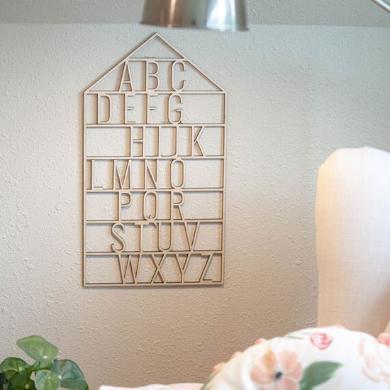 wooden alphabet house nursery decor next to a white chair, lamp, and a green plant