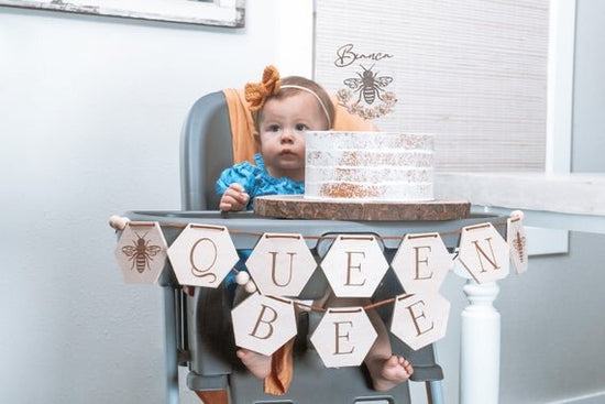 Bee Cake Topper with Flowers, birthday bee cake topper on a white cake with matching queen bee banner. With a baby in her high chair.