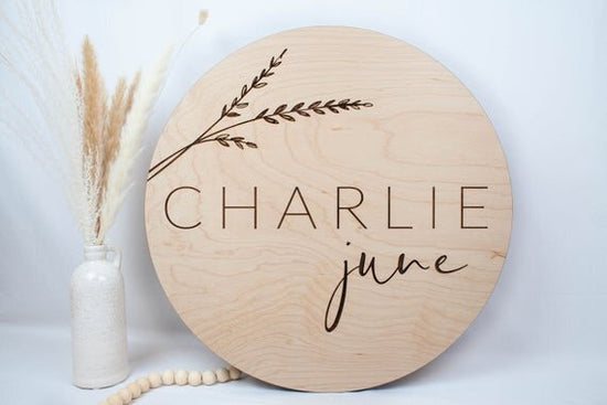 Botanical engraved wooden baby sign next to botanical plant and beads.