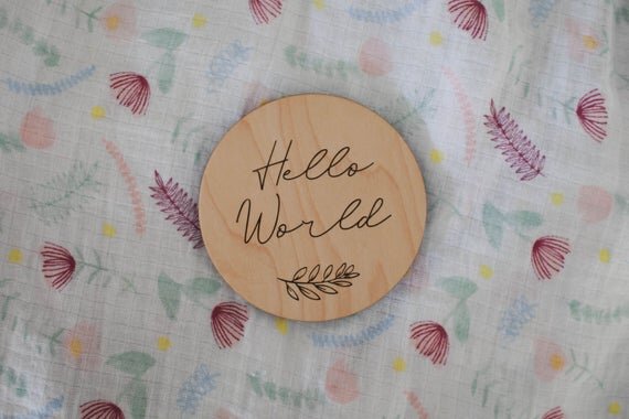 Botanical wooden baby milestone circle, hello world wooden baby circle on top of colorful sheet.