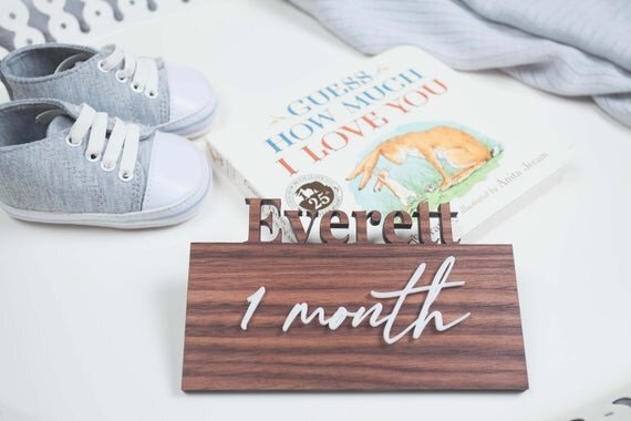 Custom wood milestone plates, 3D milestone plates next to baby shoes and book.