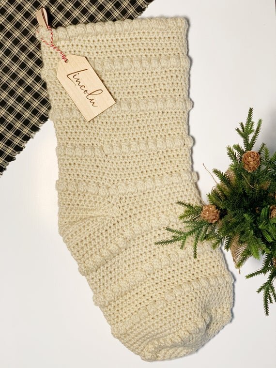 3.5" personalized wooden tags with red string on tan knitted stocking next to plaid cloth and small pine tree