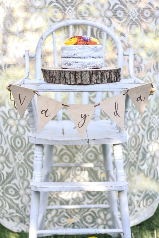 Custom banner, pennant flags on a white wooden high chair with a white cake on top.