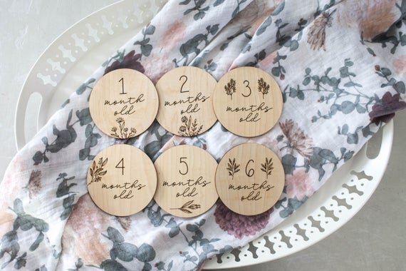 Botanical wooden baby milestone circles displayed on a white platter with floral sheet on top.