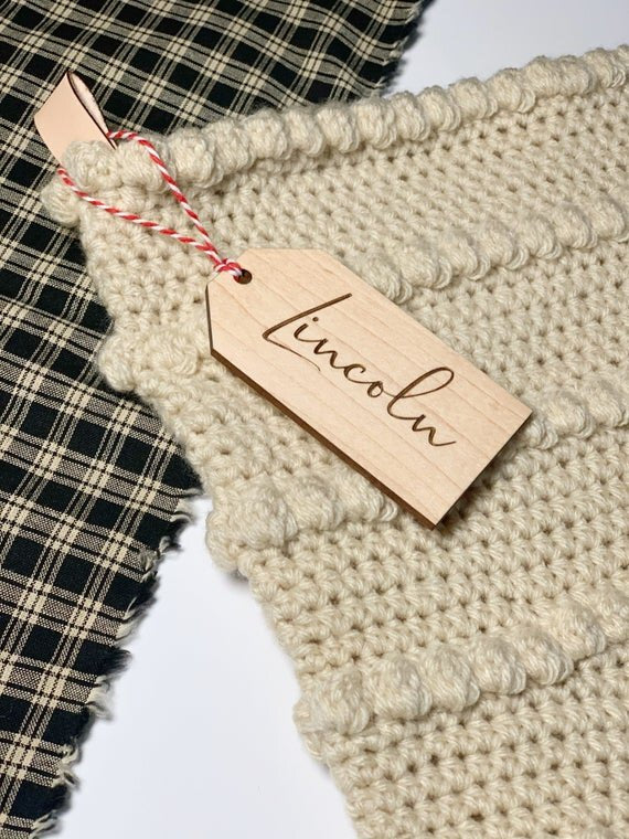 3.5" personalized wooden tags with red string on tan knitted stocking next to plaid cloth