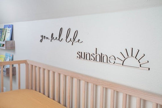 you feel like sunshine above the crib cut out sign on a white wall next to a wooden crib and shelves filled with books in the background