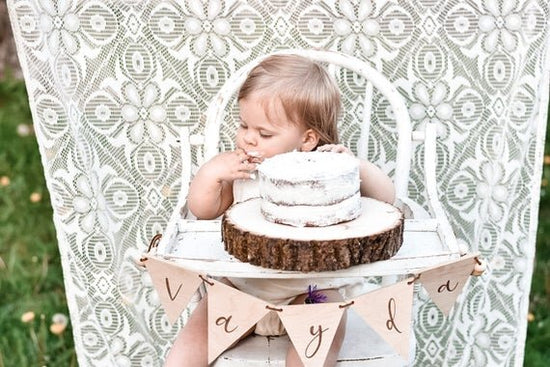 Custom banner, pennant flags on a white wooden high chair with a baby sitting on it eating a cake.