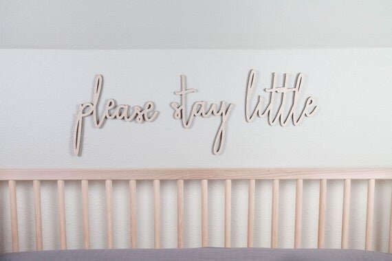 please stay little above the crib cut out sign on a white wall next to a wooden crib