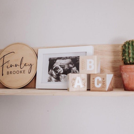 Load image into Gallery viewer, Baby name sign, welcoming home baby name sign, minimalistic birth announcement, on wooden shelf next to baby ultrasound, alphabet bricks, and a cactus.
