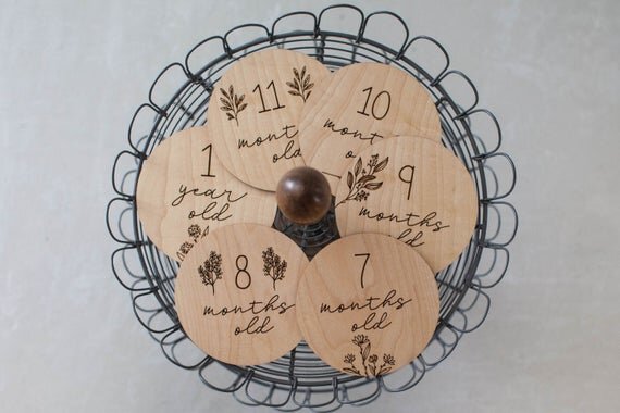 Botanical wooden baby milestone circles displayed on a black wired basket.