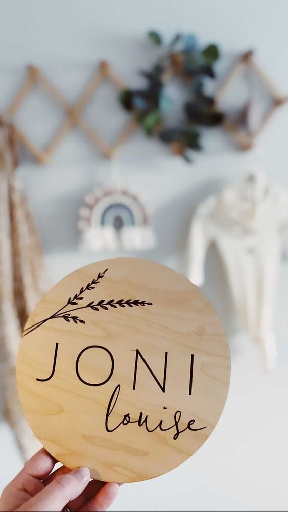 Botanical engraved wooden baby sign being held in front of babies nursery room.