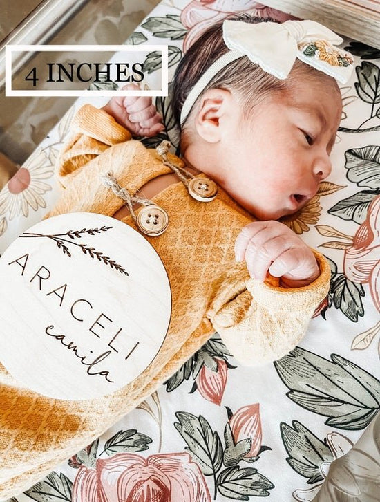 Botanical engraved wooden baby sign on top of laying newborn baby in hospital bed