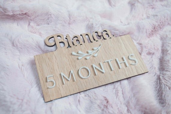Custom wooden baby milestones, 3D milestone plaques with name on a pink furry blanket.