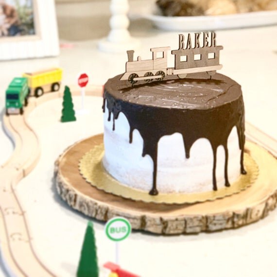 Custom train cake topper on a cake next to toy railway and train.