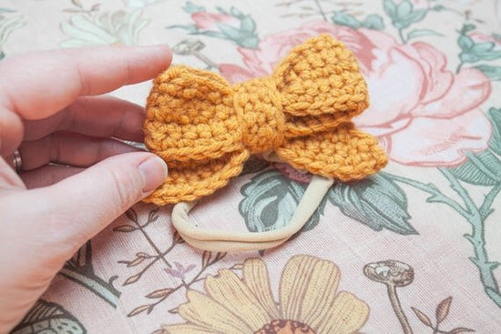 Mustard color crochet hair bow with head band being held on a hand.