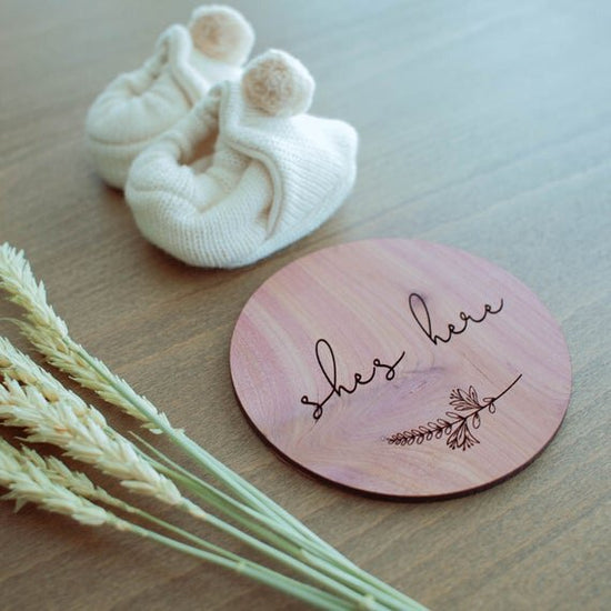 She's here red cedar wood birth announcement circle with white baby shoes and plant