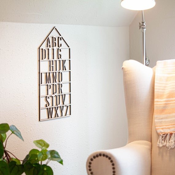 wooden alphabet house nursery decor next to white chair, a lamp that's on, and a green plant
