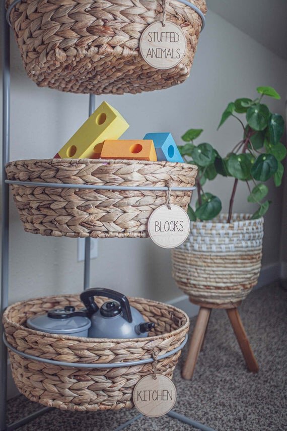 Load image into Gallery viewer, 3&amp;quot; circular wooden toy storage tags on a 3 tier wicker baskets filled with toys and green plant in the background
