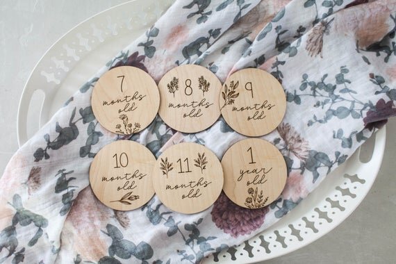 Botanical wooden baby milestone circles displayed on a white platter with floral sheet on top.