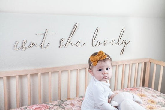 Isn't she lovely above the crib cut out sign on a white wall next to baby sitting inside a wooden crib
