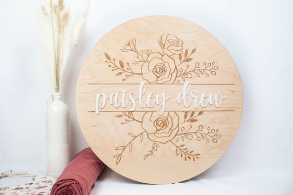 Baby Girl Nursery Sign with Floral Engraved Details next to botanical plant and baby clothes