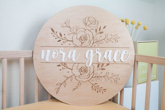 Baby Girl Nursery Sign with Floral Engraved Details inside wooden crib next to botanical plant and canvas with quote