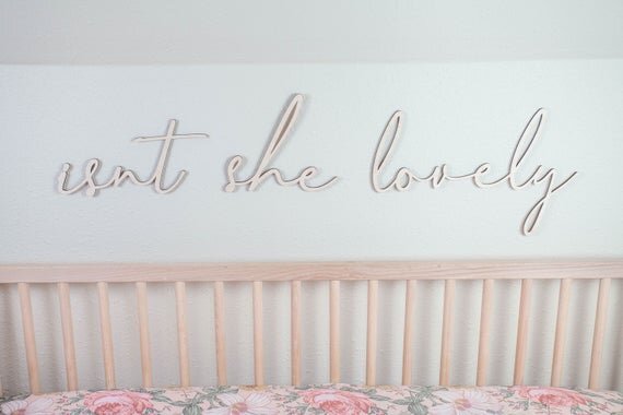 Isn't she lovely above the crib cut out sign next to a wooden crib on a white wall