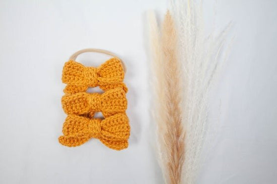 Mustard color crochet hair bows with head bands displayed next to botanical plant.