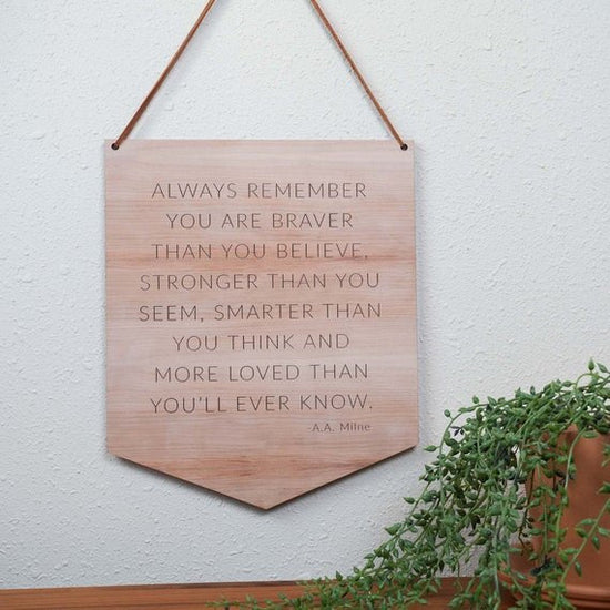 wooden nursery quote hanging on a white wall with green plants