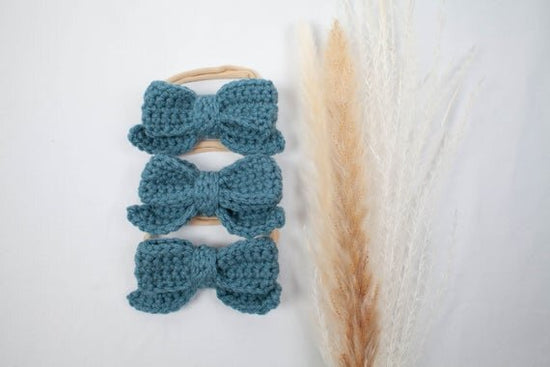 Misty blue crochet hair bows with head bands displayed next to botanical plant.