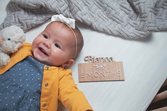 Custom wooden baby milestones, 3D milestone plaques with name next to laying down baby.