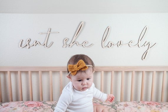 Isn't she lovely above the crib cut out sign on a white wall next to baby sitting inside wooden crib