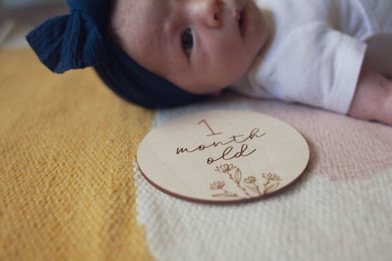 Botanical wooden baby milestone circle next to a 1 month baby laying down.